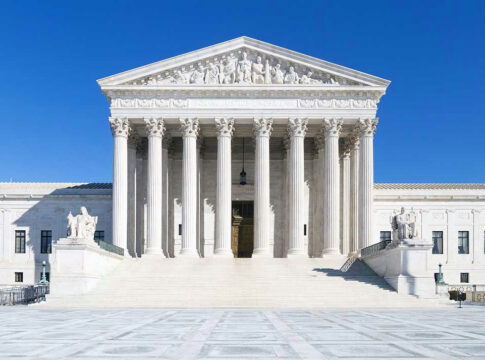 White columned building with stairs under a blue sky.