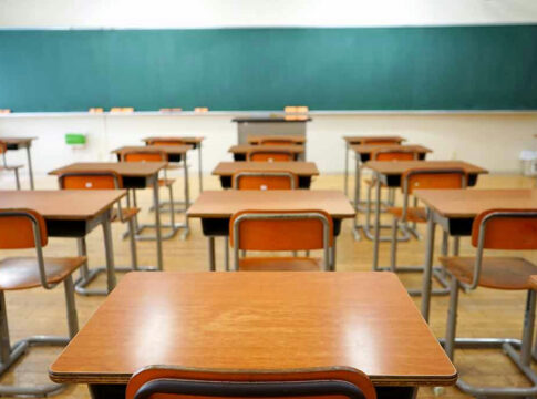 Empty classroom with wooden desks and chalkboard.