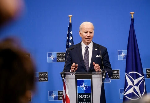 man in suit speaking at a podium with NATO backdrop