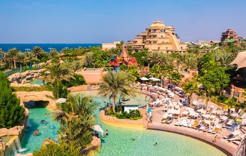 A vibrant water park with pools, palm trees, and visitors enjoying the sun