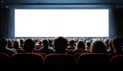 Audience seated in a dark movie theater facing a blank screen