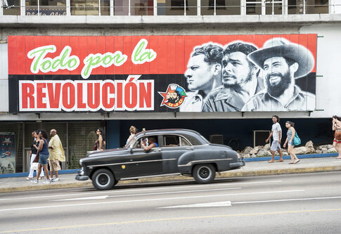 A mural depicting revolutionary figures with a classic car passing by
